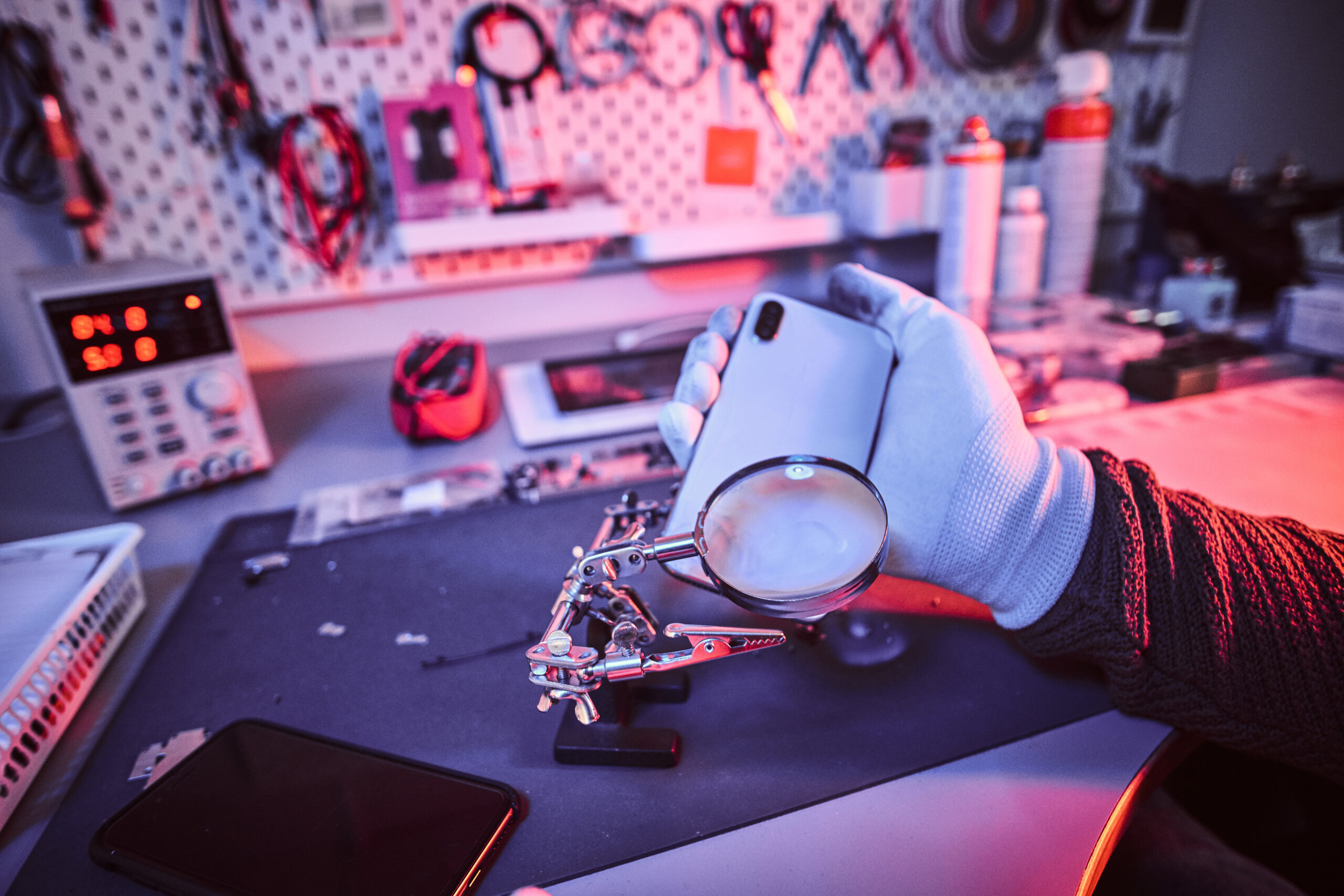 Technicien électronique tenant un smartphone cassé, entrain de l'examiner pour une réparation suite à un SAV